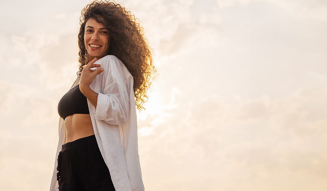 Smiling woman in stylish outfit against sunset backdrop.