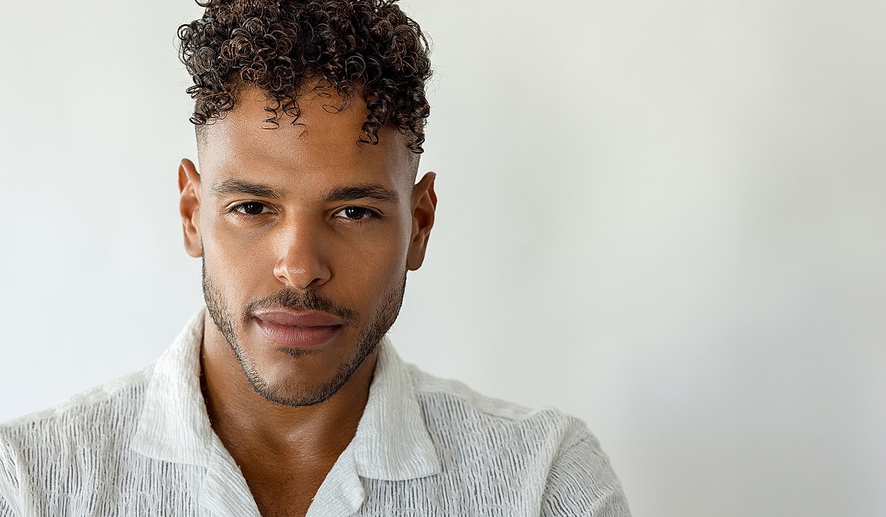 Young man with short curly hair, neutral background.