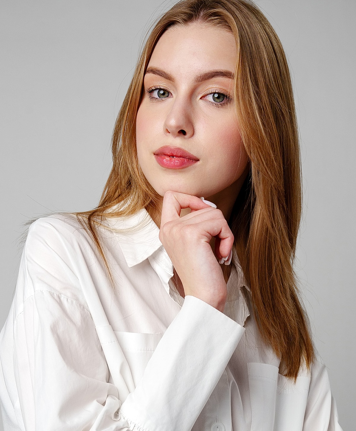 Woman in white shirt posing thoughtfully against gray.