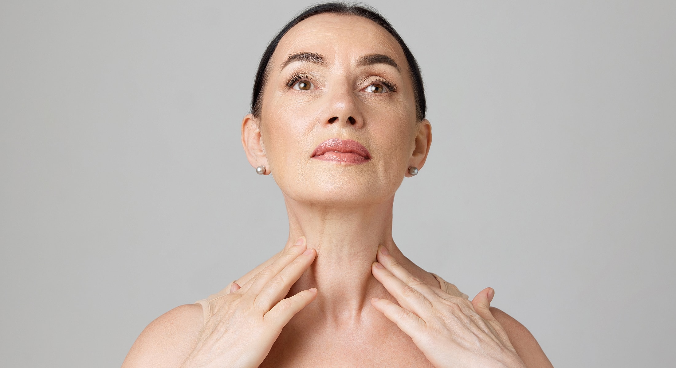 Fayetteville Neck Lift model applying skincare to her neck and jawline.